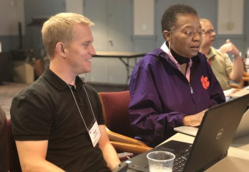 A man smiling while sitting next to a woman at a workshop.